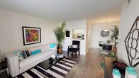 This single-floor residence offers a thoughtfully organized layout that maximizes its footprint through an efficient, open design. The living area serves as the central hub of the home, featuring rich wood-style flooring, neutral walls, and ample room for comfortable furnishings. A bold striped area rug anchors the space, complementing the clean lines of the room. A pass-through window connects the kitchen to the living and dining areas, enhancing the sense of openness and flow throughout.

The kitchen is outfitted with white cabinetry, a granite-look countertop, a stainless steel sink, and standard appliances, providing practical functionality in a compact footprint. Adjacent to the kitchen, the dedicated dining area accommodates a round table and chairs beneath a stylish pendant light fixture, creating a defined yet connected space for meals.

The bedroom offers a quieter retreat, featuring plush carpeting, a ceiling fan, and a window with natural light and outdoor views. A full bathroom serves the unit, complete with an oval vanity mirror, a single-basin sink with chrome fixtures, and a separate shower-tub area with wood-style flooring. The overall ambiance throughout is bright, clean, and cohesive.