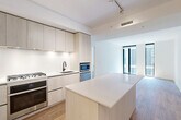This modern 2-bedroom, 2-bathroom residence at 1320 4th Street NE in Washington, DC offers a thoughtfully designed open-concept layout finished with clean, contemporary details throughout. Light wood flooring runs continuously across the living spaces, complementing the bright white walls and creating a cohesive, airy aesthetic.

The kitchen serves as the centerpiece of the main living area, featuring a large island with a white quartz countertop, light wood cabinetry extending to the ceiling, stainless steel appliances including a built-in oven and microwave, a gas cooktop, and a matte black faucet. The kitchen flows seamlessly into the combined dining and living area, which is bathed in natural light from tall, floor-to-ceiling windows framed in sleek black.

Both bedrooms are well-proportioned, each with floor-to-ceiling windows offering urban views and generous closet space, including sliding-door closets. The primary bedroom features ample room and abundant natural light. The two bathrooms are finished with distinctive hexagonal tile flooring in warm gray, white subway tile surrounds, soaking tubs, and matte black fixtures. The primary bath includes a dual-sink vanity with an integrated mirror cabinet. Additional features include in-unit laundry, a utility room, and track lighting in the kitchen.