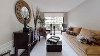 This single-floor residence offers a thoughtfully designed layout that balances comfort and functionality across multiple rooms. The living room serves as the heart of the home, featuring large sliding glass doors that open to a private balcony, flooding the space with natural light and offering pleasant outdoor views of lush greenery. Light tile flooring runs throughout the main living areas, complementing the neutral-toned walls and creating a clean, cohesive aesthetic. A sitting nook near the balcony entrance provides an inviting retreat with additional access to the outdoors. The dining area is highlighted by a contemporary pendant light fixture, wainscoting along the lower walls, and a glass-top dining table paired with a bar-height counter seating area adjacent to the kitchen. The kitchen is well-equipped with white cabinetry, dark granite countertops, white appliances, and tile flooring, offering a functional and efficient workspace. Two bathrooms feature white tile flooring, granite vanity surfaces, and vibrant wall art that adds character to each space. The bedrooms are carpeted and comfortably sized, with closet storage and windows that allow for natural light. The overall ambiance is warm and livable, with a layout that accommodates both everyday living and comfortable hosting.