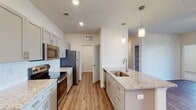 Located at 115 Beaumont Oaks Dr in Wilmington, NC, this single-floor residence offers a thoughtfully designed open-concept layout with modern finishes throughout. The kitchen is a standout feature, boasting granite countertops, gray shaker-style cabinetry, a white subway tile backsplash, stainless steel appliances — including a refrigerator, range, microwave, and dishwasher — and a large center island with a undermount sink and pendant lighting overhead. The kitchen flows seamlessly into the spacious living area, which features durable wood-look flooring, a ceiling fan, and natural light from surrounding windows. The bedrooms are carpeted for comfort, each with ceiling fans and windows that bring in natural light and outdoor views of the surrounding neighborhood. The bathrooms are finished with granite-top vanities, white cabinetry, undermount sinks, and wood-look flooring, with one bathroom featuring grab bars and a tub/shower combination. A dedicated laundry room houses a full-size GE washer and dryer with overhead wire shelving for additional storage. Throughout the residence, clean white walls, recessed lighting, and consistent finishes create a cohesive, move-in-ready aesthetic well-suited to comfortable everyday living.