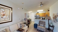 Located at 975 Woodland Village in San Marcos, Unit #169 is a thoughtfully designed single-floor residence that combines comfort and functionality. The open-concept living and dining area features light wood-style flooring, neutral wall tones, and a ceiling fan, creating a bright and welcoming atmosphere. A large area rug anchors the living space, which flows naturally into a compact dining nook bathed in natural light from a window dressed with sheer curtains.

The kitchen is well-equipped with warm honey-toned cabinetry, a full suite of appliances including a refrigerator, electric range, and microwave, and a peninsula with a double sink and countertop seating. Light wood flooring continues throughout, maintaining a cohesive look.

Both bedrooms feature plush carpeting and elegant crystal chandeliers as focal points. One bedroom includes a mirrored sliding closet door and a starburst wall mirror accent, while the other is highlighted by a natural-light window with decorative curtains and its own chandelier. Each room exudes a calm, refined ambiance.

Two bathrooms serve the unit, each with a shower/tub combination, wood-toned vanities, and efficient storage. The overall design of the unit is clean, comfortable, and move-in ready.
