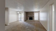 This single-floor, 2-bedroom, 2-bathroom residence offers a well-organized layout encompassing a combined kitchen and living room, two bedrooms, two bathrooms, two closets, a hallway, and an entrance. The spacious living room is a standout feature, anchored by a full-height brick fireplace with a raised hearth and mantel. Neutral-toned carpet extends throughout the living areas, complemented by a textured ceiling and a pendant light fixture. A sliding glass door floods the living room with natural light and provides access to an outdoor area. The kitchen is appointed with rich, dark wood cabinetry, granite countertops, stainless steel appliances including a range and over-the-range microwave, and wood-look flooring. A breakfast bar peninsula connects the kitchen to the living area, offering both functionality and an open feel. Each bedroom features plush carpet, a ceiling fan, and ample closet space, with one bedroom offering a built-in shelved walk-in closet. Both bathrooms include granite-topped dark wood vanities, wood-look flooring, and tiled tub-shower combinations, presenting a consistent and refined finish throughout the home.