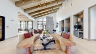 This generously proportioned single-floor amenity clubhouse is designed to impress at every turn. The grand lobby lounge anchors the space with soaring vaulted ceilings adorned with exposed wood beam detailing and dramatic pendant lighting installations that cascade downward in striking clusters. Curved, neutral-toned sofas arranged around a sculptural coffee table create an inviting central gathering area, while large-format tile flooring and floor-to-ceiling windows flood the interior with abundant natural light and outdoor views.

The space flows seamlessly into distinct functional zones. A dedicated game room features a pool table, foosball table, shuffleboard, and high-top seating, all beneath a warm wood-paneled ceiling with circular ring chandeliers. A well-appointed bar area showcases a marble-topped island with bar seating, sleek cabinetry, and globe pendant lighting. Private meeting and conference rooms with glass walls and curated artwork provide quiet retreats from the main areas.

Additional seating vignettes include built-in wood bookshelf dividers with lounge chairs, intimate upholstered booth nooks with pendant lighting, and a formal dining area with a communal wood table. Geometric-patterned area rugs, bold curated artwork, and thoughtful accent furnishings throughout lend the space a sophisticated, contemporary character.