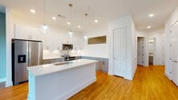 Located at 5126 Peachtree Blvd in Chamblee, Georgia, this single-floor residence offers a thoughtfully designed open layout with contemporary finishes throughout. Warm-toned hardwood flooring flows seamlessly across every room, anchoring the bright, clean aesthetic defined by crisp white walls and modern trim details.

The kitchen serves as the centerpiece of the space, featuring a large island with a white quartz countertop and undermount sink, two-tone cabinetry pairing white upper cabinets with gray lower cabinets, stainless steel appliances, and stylish globe pendant lights. Recessed lighting adds additional brightness throughout.

The living area is highlighted by a wall of large floor-to-ceiling windows that invite abundant natural light and provide views of the surrounding outdoor greenery. An elegant board-and-batten accent wall and a ceiling fan contribute to the room's refined, contemporary character.

The hallway features a built-in niche, adding a subtle architectural detail. Bedrooms are well-proportioned and include ceiling fans. The walk-in closet is outfitted with a multi-tiered shelving and hanging rod system, offering generous storage capacity.

The bathrooms are finished with gray vanity cabinetry, white quartz countertops, framed mirrors, brushed gold fixtures, and clean tile surrounds. The overall ambiance of the space is modern, light-filled, and move-in ready.