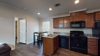 This single-story residence offers a cohesive, well-appointed interior defined by dark hardwood-style flooring and crown molding that carry consistently throughout the home. The living area serves as a welcoming entry point, featuring a ceiling fan with light fixture, a front-facing window with blinds for natural light, and ample space for comfortable seating arrangements.

The kitchen is a functional highlight of the home, centered around a peninsula island with a double sink and granite-style countertops. Rich, warm-toned cabinetry extends to the ceiling, providing generous storage. Black appliances—including a refrigerator, electric range, over-the-range microwave, and dishwasher—complete the space. Recessed lighting and a window brighten the area, while an adjacent dining space accommodates a bar-height table and stools.

The bedrooms are comfortably sized, each featuring crown molding, neutral wall tones, and windows with blinds. At least one bedroom includes a walk-in closet and ceiling fan. The two bathrooms mirror each other in design, each offering a vanity with granite-style countertops, rich wood cabinetry, a mirror, and matching dark flooring, with one bathroom including a shower.