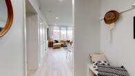 This thoughtfully designed single-floor residence combines contemporary architecture with functional living. Light hardwood flooring flows throughout, complementing the clean white walls and recessed lighting that create a bright, airy atmosphere from entry to living area.

The open entryway leads down a hallway lined with closet storage, opening into a spacious living room anchored by expansive floor-to-ceiling windows. These large-format windows flood the space with natural light and frame striking views of the surrounding urban skyline, with notable red-brick architecture visible in the distance.

The kitchen is outfitted with stainless steel appliances, including a range and over-the-range microwave, set against crisp white cabinetry, quartz countertops, and a classic subway tile backsplash — a clean, functional design suited for everyday cooking.

The bedrooms each feature a built-in wardrobe system that surrounds the bed alcove, maximizing storage while maintaining a sleek, uncluttered aesthetic. Large windows in the bedrooms continue the theme of natural light and urban views.

The bathrooms are finished with large-format light tile flooring, a modern floating vanity with an LED-backlit mirror, and a soaking tub with tiled surround, offering a spa-like atmosphere. Every room reflects a cohesive, modern design sensibility throughout this well-appointed urban residence.