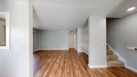 This two-story home in Napa, California offers a clean, neutral aesthetic with consistent finishes across both levels. The main living area is generously proportioned, featuring warm wood-look flooring, soft gray walls, and a textured ceiling. A standout feature is the built-in shelving and desk unit, providing functional storage and workspace within the living space. An adjacent dining area connects to the kitchen via a pass-through window with a wood ledge counter, creating an open, communicative layout. The kitchen is equipped with white cabinetry, light quartz countertops, a stainless steel sink with a pull-down faucet, and a dishwasher, with a large window offering views of surrounding greenery.

The bedrooms are carpeted and finished in the same soft gray palette, with windows that admit natural light and outdoor views of mature trees. Two bathrooms serve the home, each featuring wood-look flooring, white tile tub-and-shower surrounds, and gray vanities with white countertops and brushed nickel fixtures. The overall ambiance is bright, well-maintained, and move-in ready, with a cohesive design throughout.