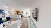 This single-floor residence showcases a thoughtfully designed open-concept layout with a contemporary aesthetic throughout. The kitchen is equipped with stainless steel appliances, including a side-by-side refrigerator, electric range, and built-in microwave, all complemented by sleek dark wood cabinetry and a white quartz island. An in-unit washer and dryer are conveniently tucked into a dedicated laundry alcove nearby.

The living area features wood-style flooring, a ceiling fan, and sliding glass doors that open onto a private balcony, allowing natural light to fill the space and providing outdoor views of surrounding greenery. The room offers generous wall space suitable for large-format artwork or a mounted television.

Multiple bedrooms are finished with plush carpeting, ceiling fans, and windows that bring in natural light. At least one bedroom includes a walk-in closet with built-in shelving. The bathroom presents a clean, white palette with tile surround, a soaking tub and shower combination, a floating vanity, and marble-style flooring.

Overall, the space maintains a modern, neutral tone with crisp white walls and consistent finishes, creating a cohesive and functional living environment.