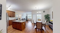 Located at 1 Courtney Way in Mount Laurel, NJ, this well-appointed 2-bedroom, 2-bathroom residence offers a thoughtfully designed single-floor layout. The open-concept living, dining, and kitchen area forms the heart of the home, with warm hardwood-style flooring flowing throughout. The kitchen is equipped with rich cherry-toned cabinetry, granite countertops, stainless steel appliances, a tile backsplash, and a central island with seating — ideal for both cooking and casual dining. The adjacent dining area is illuminated by an elegant chandelier and benefits from large windows that invite abundant natural light. The living room provides a comfortable, relaxed atmosphere with additional window views. The spacious primary bedroom features plush carpeting, a walk-in closet, and direct access to a private en-suite bathroom complete with a dual-sink vanity, tile flooring, and a glass-enclosed shower. The second bedroom is equally comfortable, with carpet, a large window, and convenient access to the second full bathroom, which includes a single vanity and tile flooring. A hallway and closet round out the floor plan, providing practical storage. The overall ambiance is clean, bright, and move-in ready.