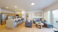 Located at 399 S. Crouse Ave in Syracuse, NY, this well-designed single-floor unit offers a thoughtfully organized layout across six rooms. The open-concept living and kitchen area serves as the heart of the space, where light wood-toned cabinetry, stainless steel appliances, and a sleek white quartz breakfast bar with bar seating define a modern, functional kitchen. Light hardwood flooring flows seamlessly throughout, enhancing the bright, airy atmosphere created by recessed lighting and large windows. The living room comfortably accommodates a full seating arrangement and features large sliding glass doors that open onto a private balcony, offering views of the surrounding building courtyard and filling the space with natural light. Two bedrooms provide comfortable private retreats, each with windows that bring in additional daylight. Two bathrooms, each featuring a shower and clean, minimalist finishes with ample vanity storage, serve the unit. The overall design aesthetic is contemporary and cohesive, with neutral white walls, consistent flooring, and modern fixtures throughout. The unit's efficient layout makes excellent use of its footprint, providing a comfortable and practical living environment well-suited to residents near Syracuse University.