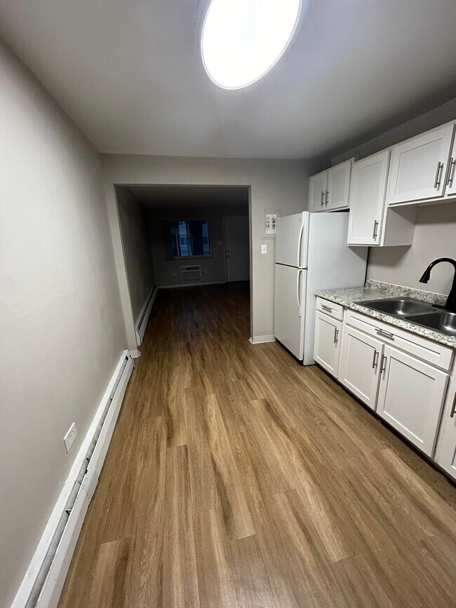 Modern kitchen with sleek granite countertops, white cabinetry, and warm wood flooring extending into a cozy living area. - 7030 Stuart St and 4260 W 70th