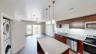 This 2-bedroom, 2-bathroom residence in Cedar Park, Texas offers a thoughtfully designed open-concept layout that connects the kitchen, dining, and living areas seamlessly. The kitchen is a standout feature, showcasing rich dark-wood cabinetry, granite countertops, a large center island with pendant lighting, a classic subway tile backsplash, and a full suite of stainless steel appliances. Wood-style flooring runs throughout the main living areas, adding warmth and cohesion to the space.

The living room is bright and airy, equipped with a ceiling fan and direct access to a private balcony through sliding glass doors, offering expansive outdoor views of the surrounding landscape. The primary bedroom is generously sized, featuring plush carpet, a ceiling fan, and access to its own bathroom. The second bedroom also features carpet flooring and is conveniently located near the second full bathroom.

Both bathrooms are well-finished, featuring granite-topped vanities with dark wood cabinetry and tiled tub-shower combinations with brushed nickel fixtures. The unit also includes an in-unit washer and dryer, as observed in the floor plan view. Neutral wall tones throughout create a clean, modern ambiance suitable for a variety of décor styles.