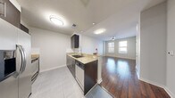 This well-designed single-floor residence offers a thoughtful open-concept layout that seamlessly connects the kitchen and living areas. The kitchen is outfitted with dark espresso cabinetry, granite countertops, a stainless steel appliance suite including a refrigerator, dishwasher, and range, complemented by a subway tile backsplash and light tile flooring. A peninsula counter opens directly to the living area, enhancing the sense of flow throughout the space.

Rich, dark hardwood flooring extends across the living room, hallway, and bedrooms, providing a warm contrast to the neutral-toned walls. The living area benefits from natural light streaming through large windows fitted with horizontal blinds, and a ceiling fan adds both style and function overhead.

The bedroom features dual windows that frame striking city skyline views, offering an urban backdrop filled with natural light. A dedicated hallway connects the bedroom to the bathroom and closet space, maintaining a clean and organized traffic flow.

The bathroom is finished with neutral tile flooring, a soaking tub with a tiled surround, and dark wood vanity cabinetry that mirrors the kitchen's design language. Throughout the residence, the consistent use of materials and a cohesive neutral color palette create a polished, modern ambiance.