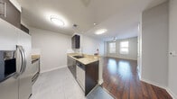 This well-designed single-floor residence offers a thoughtful open-concept layout that seamlessly connects the kitchen and living areas. The kitchen is outfitted with dark espresso cabinetry, granite countertops, a stainless steel appliance suite including a refrigerator, dishwasher, and range, complemented by a subway tile backsplash and light tile flooring. A peninsula counter opens directly to the living area, enhancing the sense of flow throughout the space.

Rich, dark hardwood flooring extends across the living room, hallway, and bedrooms, providing a warm contrast to the neutral-toned walls. The living area benefits from natural light streaming through large windows fitted with horizontal blinds, and a ceiling fan adds both style and function overhead.

The bedroom features dual windows that frame striking city skyline views, offering an urban backdrop filled with natural light. A dedicated hallway connects the bedroom to the bathroom and closet space, maintaining a clean and organized traffic flow.

The bathroom is finished with neutral tile flooring, a soaking tub with a tiled surround, and dark wood vanity cabinetry that mirrors the kitchen's design language. Throughout the residence, the consistent use of materials and a cohesive neutral color palette create a polished, modern ambiance.