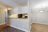 This single-floor residence offers a practical and cohesive layout with a warm, neutral color palette throughout. Rich wood-look flooring flows through the main living and kitchen areas, complemented by clean white baseboards and textured ceilings that add understated character to each room.

The kitchen is a functional galley-style space equipped with dark cabinetry, granite-style countertops, a double stainless steel sink, and black appliances including a refrigerator and electric range. A pass-through window connects the kitchen to the adjacent living area, promoting an open and connected feel.

The living areas are well-lit by natural light streaming through slatted blinds on multiple windows and glass doors, creating a bright and welcoming atmosphere. One of the main living spaces features a set of glass panel doors that open to the exterior, adding a seamless indoor-outdoor connection.

The bedrooms include one with soft carpeting and another with wood-look flooring, each offering a quiet and comfortable retreat. A generous walk-in closet with wire shelving provides ample storage. The bathroom features a full soaking tub with a clean white surround and a brushed nickel grab bar, combining functionality with a tidy, modern aesthetic.