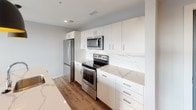 This thoughtfully designed 1-bedroom, 1-bathroom residence offers a clean, modern aesthetic throughout. The open-concept living area features durable wood-style flooring and is bathed in natural light, courtesy of large sliding glass doors that open onto a private balcony with panoramic views of the surrounding neighborhood and skyline. The kitchen is outfitted with stainless steel appliances—including a refrigerator, electric range, and over-the-range microwave—complemented by sleek white cabinetry, ample storage, and striking marble-veined quartz countertops and backsplash that lend a polished, upscale feel. A stylish barn-style door adds a distinctive architectural touch to the interior. The bedroom is a comfortable retreat, carpeted for warmth and comfort, with two large windows that frame elevated city views and fill the room with abundant natural light. The bathroom is clean and functional, featuring a full soaking tub and shower combo with chrome fixtures set against crisp white walls. Throughout the residence, a neutral color palette and contemporary finishes create a cohesive, inviting ambiance that is both modern and livable.
