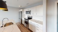 This thoughtfully designed 1-bedroom, 1-bathroom residence offers a clean, modern aesthetic throughout. The open-concept living area features durable wood-style flooring and is bathed in natural light, courtesy of large sliding glass doors that open onto a private balcony with panoramic views of the surrounding neighborhood and skyline. The kitchen is outfitted with stainless steel appliances—including a refrigerator, electric range, and over-the-range microwave—complemented by sleek white cabinetry, ample storage, and striking marble-veined quartz countertops and backsplash that lend a polished, upscale feel. A stylish barn-style door adds a distinctive architectural touch to the interior. The bedroom is a comfortable retreat, carpeted for warmth and comfort, with two large windows that frame elevated city views and fill the room with abundant natural light. The bathroom is clean and functional, featuring a full soaking tub and shower combo with chrome fixtures set against crisp white walls. Throughout the residence, a neutral color palette and contemporary finishes create a cohesive, inviting ambiance that is both modern and livable.