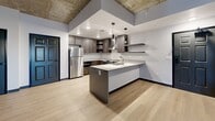 Located at 215-219 S Water St in Henderson, NV, this 3-bedroom, 2-bathroom residence offers a thoughtfully designed single-level layout with a striking industrial-modern aesthetic. Exposed concrete ceilings contrast beautifully with clean white walls and light-toned luxury vinyl plank flooring found throughout the main living areas, creating a bold yet refined atmosphere.

The kitchen serves as a central highlight, featuring dark wood cabinetry, stainless steel appliances including a range and refrigerator, a wall-mounted range hood, and a peninsula island with a sink and pendant lighting above — ideal for both cooking and casual dining.

The living area benefits from a private balcony accessible via a glass-paned door, allowing natural light to flow in alongside views of the surrounding landscape. Each of the three bedrooms offers a comfortable, carpeted retreat with exposed concrete ceilings and windows that frame outdoor views. The spacious primary bedroom includes a dedicated walk-in closet with wrap-around shelving and hanging rods.

Both bathrooms are finished in a clean, contemporary style with large-format tile flooring, floating dark wood vanities, illuminated medicine cabinet mirrors, and tub-shower combinations with brushed nickel fixtures — delivering a polished, hotel-inspired feel throughout.