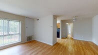 This single-floor residence offers a practical and comfortable layout across several distinct living areas. The main living space is anchored by warm hardwood flooring that extends throughout the common areas, complemented by neutral-toned walls and a ceiling fan that adds to the airy feel. A large window with vertical blinds allows natural light to pour into the living room, offering views of lush greenery outside.

The kitchen is well-equipped, featuring warm oak cabinetry, dark granite-style countertops, and a matching dark backsplash that ties the space together. Black appliances — including a gas range, dishwasher, and under-cabinet range hood — give the kitchen a cohesive, functional aesthetic. A stainless steel sink sits beneath an additional window, further brightening the workspace.

The bedrooms are carpeted, providing a softer underfoot feel, and each offers generous proportions with ample wall space. One bedroom includes a large window with outdoor views, while another features a built-in closet with bifold doors, conveniently located near the unit entrance.

The bathroom is neatly appointed with hardwood-style flooring, an oak vanity with a white countertop, and an oval mirror with overhead lighting, creating a clean and functional space. A hallway connects all areas, contributing to a smooth and logical flow throughout the residence.