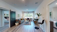 This well-appointed single-floor residence offers a thoughtfully designed open-concept layout that seamlessly connects the main living areas. The living room is bright and welcoming, featuring light wood-style flooring, large windows that invite an abundance of natural light, and a sliding barn door accent that adds a contemporary touch. A glass-top coffee table and colorful area rug anchor the seating area, complemented by views of lush greenery outside.

The kitchen is a functional centerpiece of the home, outfitted with grey shaker-style cabinetry, speckled granite countertops, and a full suite of stainless steel appliances including a refrigerator, range, and over-the-range microwave. A central island with seating provides additional prep space and a casual dining option, with pendant lighting overhead adding a refined finishing touch.

The bedrooms offer a tranquil retreat, each with plush carpeting, windows allowing natural light, and ample closet space. The bathrooms mirror the kitchen's aesthetic with matching grey cabinetry, granite vanity tops, gold-toned fixtures, and light wood-style flooring. Throughout the residence, a consistent neutral color palette, recessed lighting, and quality finishes create a cohesive, modern atmosphere that is both functional and visually appealing.