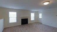 This single-floor residence offers a clean and functional layout designed for comfortable everyday living. The main living area is generously proportioned, featuring light-toned carpeting and smooth, neutral-painted walls that create a bright and airy atmosphere throughout. A classic fireplace with a simple white mantel serves as the focal point of the living room, framed by multiple windows that allow abundant natural light to fill the space. The windows provide views of the surrounding outdoor greenery, enhancing the sense of openness and connection to the exterior. A glass-paneled entry door adds additional light to the room while offering a welcoming point of entry. The ceiling is smooth and well-lit with a flush-mounted light fixture, contributing to the clean, understated aesthetic of the space. The overall design is neutral and versatile, providing an excellent canvas for a variety of interior styles. The single-story layout ensures easy accessibility and seamless flow throughout the home, making it a practical and inviting living environment.