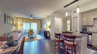 This single-floor residence offers a thoughtfully designed open-concept layout that seamlessly connects the main living areas. The living room is a welcoming space featuring dark hardwood flooring, a ceiling fan, and floor-to-ceiling sliding doors that flood the room with natural light and provide access to an outdoor balcony with views of surrounding greenery. A breakfast bar with granite countertops and pendant lighting bridges the living area and kitchen, providing convenient seating for casual dining.

The kitchen is well-equipped with stainless steel appliances, light wood cabinetry extending to the ceiling for ample storage, granite countertops, and a striking mosaic tile backsplash. A separate dining area off the main living space features dark hardwood floors and offers a defined setting for more formal meals.

The primary bedroom is carpeted and distinguished by a bold accent wall, dual windows, and a ceiling fan, creating a comfortable and restful retreat. A second bedroom mirrors the cozy feel with plush carpet, natural light from a large window, and a ceiling fan. The bathroom features a clean, modern aesthetic with large-format tile, an open walk-in shower with a built-in bench, matte black fixtures, and a dark vanity with granite countertops.
