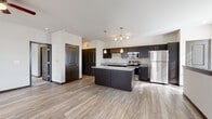This single-floor residence offers a well-designed, open-concept layout that seamlessly connects the kitchen and living areas. The kitchen is a standout feature, equipped with dark espresso cabinetry, granite countertops, and a full suite of stainless steel appliances including a refrigerator, range, and built-in microwave. A central island with matching granite provides additional prep and seating space, while a combination of pendant lights and a track lighting fixture above adds focused illumination. A built-in wine rack accent adds a distinctive touch to the upper cabinetry.

Wood-style plank flooring extends throughout the main living areas, complementing the contemporary color palette of neutral walls and dark trim. The living area receives natural light through large windows fitted with horizontal blinds. Bedrooms feature plush carpeting, generous windows, and access to closet space, maintaining a comfortable and functional atmosphere. Dark-paneled interior doors are consistent throughout, contributing to a cohesive design aesthetic.

The bathroom includes a full tub-shower combination, a dark vanity with granite countertop, and wood-style flooring that mirrors the rest of the unit. Overall, the space presents a modern, well-appointed environment with consistent finishes throughout.