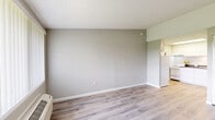 This single-floor unit offers a straightforward, functional layout with consistent design elements throughout. The main living area is finished with light wood-style vinyl flooring and neutral gray textured walls, complemented by white baseboards and a textured popcorn ceiling. A large window fitted with vertical blinds allows natural light to fill the space while offering an open outdoor view, and a wall-mounted PTAC heating and cooling unit ensures year-round climate control.

The compact kitchen is efficiently arranged and features white shaker-style cabinetry, dark countertops, a single-basin sink with a gold-toned faucet, and a white electric range and refrigerator. A skylight above the kitchen provides additional natural illumination, enhancing the brightness of the space.

The bathroom includes a built-in tub and shower combination with chrome and gold-toned towel bars and a grab bar for added convenience. Additional rooms provide versatile spaces with the same cohesive flooring and neutral wall tones, with closet access adding practical storage. Overall, the unit presents a clean, move-in-ready environment with a consistent, understated aesthetic throughout.
