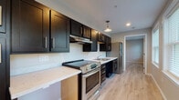 Located at 31 Village Lane in Groton, Connecticut, this thoughtfully designed single-floor unit offers a clean, modern aesthetic throughout. Light-toned wood plank flooring runs continuously across the space, creating a cohesive and bright interior that complements the neutral warm-gray wall palette.

The kitchen is a standout feature, showcasing rich dark espresso cabinetry with sleek bar-pull hardware, light quartz countertops, and a full suite of stainless steel appliances including an electric range and refrigerator. An under-cabinet range hood and a pendant light overhead add both functionality and style. Notably, an accessible open section of countertop is integrated into the kitchen design, reflecting thoughtful universal design principles.

The open living and dining area benefits from multiple windows that invite generous natural light and views of the surrounding greenery. A pendant light fixture and a wall-mounted ductless HVAC unit provide comfort and ambiance, while a glass-panel entry door enhances the connection to the outdoors.

The bedroom areas are spacious and versatile, with angled ceiling details adding architectural character. The bathroom is fully ADA-accessible, equipped with grab bars at the vanity, toilet, and walk-in shower, a wide-format layout, and light, easy-care finishes throughout. This unit combines accessibility, modern finishes, and functional design in a cohesive and move-in-ready package.