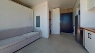 Located at 1520 Tyler, Unit 301, in San Diego's 92103 zip code, this efficiently designed studio apartment spans 170 square feet across a single floor. The open-concept main living area integrates a fully equipped kitchen and living space, finished with polished concrete floors and exposed concrete block walls that lend a contemporary, industrial aesthetic. The kitchen features white cabinetry with dark hardware, a butcher block countertop, stainless steel appliances including a refrigerator and range, a single-basin sink, and white tile backsplash. A large sliding glass door floods the space with abundant natural light and opens directly onto a private balcony, which is enclosed by a horizontal wood-slat railing and offers open views of the San Diego skyline and neighborhood under characteristically sunny Southern California skies. The living area accommodates a sofa and includes a space-saving wall-mounted Murphy bed, maximizing functionality within the compact footprint. A separate bathroom features a corner glass-enclosed shower with black framing, a white vanity, and clean white finishes throughout. A bold dark entry door and in-unit washer hookup complete this smartly appointed urban studio.