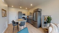 This single-floor residence showcases a thoughtfully designed open-concept layout with light wood flooring throughout. The kitchen serves as a central highlight, featuring two-tone cabinetry in charcoal grey and natural wood, complemented by a full suite of stainless steel GE appliances including a French door refrigerator, electric range, and over-the-range microwave. A large central island with a quartz-style countertop provides seating for several bar-height chairs, making it ideal for casual dining and entertaining. Ample upper and lower cabinetry ensures generous storage.

The living area benefits from floor-to-ceiling sliding glass windows that frame expansive urban views, flooding the space with natural light. Two well-proportioned bedrooms feature the same warm wood flooring, neutral walls, and windows overlooking the cityscape, creating a calm and restful atmosphere. The full bathroom is cleanly finished with a grey vanity, undermount sink, and a tiled shower-tub combination. A dedicated utility room houses a stacked GE washer and dryer alongside a water heater, providing convenient in-unit laundry. The overall aesthetic is modern, clean, and cohesive.