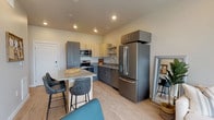 This single-floor residence showcases a thoughtfully designed open-concept layout with light wood flooring throughout. The kitchen serves as a central highlight, featuring two-tone cabinetry in charcoal grey and natural wood, complemented by a full suite of stainless steel GE appliances including a French door refrigerator, electric range, and over-the-range microwave. A large central island with a quartz-style countertop provides seating for several bar-height chairs, making it ideal for casual dining and entertaining. Ample upper and lower cabinetry ensures generous storage.

The living area benefits from floor-to-ceiling sliding glass windows that frame expansive urban views, flooding the space with natural light. Two well-proportioned bedrooms feature the same warm wood flooring, neutral walls, and windows overlooking the cityscape, creating a calm and restful atmosphere. The full bathroom is cleanly finished with a grey vanity, undermount sink, and a tiled shower-tub combination. A dedicated utility room houses a stacked GE washer and dryer alongside a water heater, providing convenient in-unit laundry. The overall aesthetic is modern, clean, and cohesive.