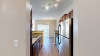 This one-bedroom, one-bathroom residence in Germantown, Tennessee offers a thoughtfully designed single-floor layout that makes efficient use of its space. The open-concept kitchen and living area form the heart of the home, where rich, warm-toned wood cabinetry pairs with granite-style countertops and a full suite of stainless steel appliances, including a refrigerator, range, and built-in microwave. Track lighting illuminates the kitchen, while a peninsula counter provides a natural transition into the living area. The living room features soft carpeting, a textured ceiling, and large windows that invite natural light and outdoor views. The bedroom is a comfortable retreat, finished with plush carpet, a ceiling fan with light fixture, and a generous walk-in closet outfitted with built-in shelving and hanging rods for ample storage. The full bathroom is clean and functional, showcasing wood-look flooring, a white vanity with a single sink and mirror, and a tiled shower-tub combination. A hallway connects the living spaces with ease, completing a practical and cohesive floor plan well-suited for comfortable everyday living.