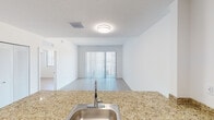Located at 13735 SW 262nd St in Homestead, Florida, this single-floor unit offers a clean, modern design with a bright and airy ambiance throughout. The open-concept living and dining area is bathed in natural light, courtesy of sliding glass doors fitted with vertical blinds that lead to an outdoor view, creating a seamless connection between interior and exterior spaces. Light wood-look flooring runs consistently throughout, complementing the crisp white walls and lending a cohesive, contemporary feel to the entire unit.

The kitchen is a functional highlight, featuring dark espresso cabinetry paired with granite countertops and a peninsula with a stainless steel sink. Stainless steel appliances — including a refrigerator, range, and over-the-range microwave — complete the well-appointed cooking space. The kitchen opens directly to the living area, making the layout ideal for everyday living and entertaining.

The bedroom is generously proportioned, with a large window that fills the room with natural light and offers outdoor views. Louvered closet doors provide practical storage.

The bathroom mirrors the design language of the rest of the unit, with a granite-topped vanity, dark cabinetry, a large wall mirror, and clean white fixtures. A dedicated closet area is also accessible from the main corridor, adding to the overall storage capacity of this thoughtfully designed space.