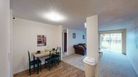 This single-floor unit offers a practical and efficiently arranged layout accommodating four bedrooms and one bathroom. The entrance leads into a combined living and dining area, where wood-look flooring defines the dining space and transitions to carpet in the living room. The living room features a large sliding glass door fitted with vertical blinds, allowing natural light to filter in while providing views of the surrounding greenery. A structural column separates the dining and living zones, adding subtle architectural definition to the open-plan area.

The kitchen is positioned adjacent to the main living space and features wood-look flooring, dark wood cabinetry, a white electric range, a dishwasher, and a window overlooking outdoor greenery. A hallway connects the living areas to the four bedrooms, each finished with neutral carpet and textured ceilings. The bedrooms are modestly sized, with the primary bedroom offering a louvered closet door. An additional dedicated closet features built-in shelving for supplemental storage. The shared bathroom includes a granite-top vanity with wood cabinetry, a shower-tub combination, and a mirrored medicine cabinet, completing this functional and straightforward layout.
