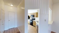 This single-floor residence offers a practical and well-organized layout designed for comfortable everyday living. The kitchen is a standout feature of the home, showcasing warm honey-toned wood cabinetry that lines both the upper and lower walls, providing generous storage space. Black appliances, including an electric range and over-the-range microwave, offer a bold contrast against the light-colored countertops and bright white walls. A stainless steel sink is positioned to complete the functional workspace. Light hardwood flooring runs through the kitchen, lending warmth and continuity to the space. Crown molding adds a subtle architectural detail to the adjoining hallway, which features neutral tile flooring that transitions smoothly into the rest of the home. The interiors are bathed in bright, even lighting, contributing to an open and airy feel. The clean white walls throughout serve as a neutral backdrop, making the space feel fresh and easy to personalize. Overall, the home presents a straightforward, move-in-ready environment with classic finishes and a cohesive design sensibility that balances practicality with comfort.
