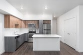 This contemporary single-floor residence offers a thoughtfully designed layout that balances functionality with modern aesthetics. The open-concept kitchen serves as the heart of the home, showcasing two-tone cabinetry with warm wood-grain upper cabinets and sleek gray lower cabinets, complemented by crisp white quartz countertops and a generously sized central island. Stainless steel appliances, including a refrigerator, range, microwave, and dishwasher, complete the kitchen's polished, move-in-ready appeal. Recessed lighting illuminates the space, while large windows allow natural light to pour into the adjacent living area.

Rich hardwood-style flooring runs throughout the main living and kitchen areas, extending into the hallway, which leads to the private quarters of the home. The bedrooms feature neutral-toned carpet, creating a comfortable and quiet retreat. The hallway also provides access to closets, offering practical storage solutions.

The residence includes two full bathrooms. The first features a single vanity with gray cabinetry, white countertop, and a tub-shower combination with clean white tile surround. The second, more spacious bathroom offers a dual-sink vanity with ample counter space, a large mirror, and a separate walk-in glass shower, making it ideal as a primary bath. Both bathrooms carry the consistent hardwood-style flooring for a cohesive look throughout the home.