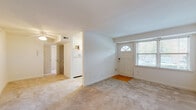 This single-floor residence offers a straightforward and functional layout, as illustrated by the 3D floor plan. The open living area serves as the heart of the unit, featuring neutral-toned wall-to-wall carpeting, crisp white walls, and a front entry door with a fan-shaped transom window that draws in natural light. An adjacent secondary entry provides added convenience. The living space flows toward the kitchen, which is separated by a partial wall and equipped with white cabinetry, a coil-burner electric range, an over-range microwave, a dishwasher, a stainless steel sink, and a window overlooking the outdoors. The space benefits from a practical, efficient design well-suited for everyday use. The bedrooms are carpeted and generously proportioned, each featuring a ceiling fan with a light fixture and windows fitted with blinds that allow for adjustable natural light. The primary bedroom includes a tray ceiling detail, adding a subtle architectural touch. The bathroom is finished in clean white tile, with a single vanity, large mirror, and a tub-shower combination enclosed by sliding glass doors. Throughout, the interior maintains a consistent, neutral aesthetic that provides a bright and functional living environment.