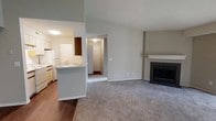This single-floor, 2-bedroom, 2-bathroom home in Water Mill offers a thoughtfully designed open layout that maximizes comfort and functionality. The living area is spacious and inviting, anchored by a classic fireplace with a white mantel surround that serves as a natural focal point. Vaulted ceilings in the living space add a sense of airiness and height, complementing the neutral-toned carpet that extends throughout the main living and bedroom areas. The kitchen is positioned adjacent to the living room, separated by a convenient breakfast bar or pass-through counter, making it ideal for entertaining. It is equipped with essential appliances, including a refrigerator, and features ample cabinetry for storage. Hardwood-style flooring in the kitchen area provides a practical contrast to the carpeted living spaces. A hallway connects the living area to the bedrooms and additional rooms, ensuring a smooth and logical flow throughout the home. The overall color palette is light and neutral, with soft gray walls and white trim, creating a clean, welcoming ambiance throughout. This well-proportioned home offers a comfortable and practical living environment in Water Mill.
