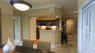 This single-floor residence showcases an open-concept layout that seamlessly connects the kitchen, dining, and living areas. The kitchen is a standout feature, equipped with rich dark wood cabinetry, granite countertops, and stainless steel appliances, including a refrigerator, microwave, and range. Under-cabinet lighting adds a warm ambiance, complementing the neutral beige walls throughout the space.

A peninsula with bar-height seating serves as both a functional workspace and a casual dining spot, bridging the kitchen and adjacent areas. Crown molding along the ceilings adds an elegant architectural detail that enhances the refined character of the space.

The dining area accommodates a full table and chairs, positioned beneath a prominent ceiling-mounted light fixture that anchors the space. Carpeted flooring flows through the living areas, while the kitchen features hard surface flooring for practicality.

An arched doorway visible in the background lends a classic architectural touch, leading to additional rooms. The overall ambiance is warm and inviting, with recessed lighting and thoughtful design choices creating a cohesive, comfortable environment throughout.