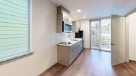 Located at 4128 36th Ave SW in Seattle's West Seattle neighborhood, this compact studio unit offers a thoughtfully designed, single-floor layout that maximizes every square foot. The open-plan living space combines the dining, kitchen, and living areas into one cohesive room, creating a sense of openness despite the efficient footprint. Warm wood-look vinyl flooring runs throughout, complementing the clean white walls and recessed lighting overhead.

The kitchen is well-appointed with contemporary gray wood-grain cabinetry — both upper and lower — paired with a white countertop, a single-basin stainless steel sink, a smooth cooktop, an over-the-range stainless steel microwave, and a full-size stainless steel refrigerator. A white tile backsplash adds a polished finish. Natural light enters through multiple windows fitted with horizontal blinds, and a sliding glass door opens to an outdoor area, offering views of the surrounding neighborhood.

The living area is bright and open, with a secondary window providing additional natural light. A dedicated closet offers practical storage, while the bathroom features a walk-in shower stall with chrome fixtures and wood-look tile flooring. The unit's clean, modern aesthetic and efficient design make it a functional and contemporary urban living space.