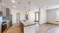 This 1-bedroom, 1-bathroom unit offers a thoughtfully designed open-concept floor plan that maximizes every square foot. Light wood-style flooring flows consistently throughout, creating a clean, cohesive aesthetic across all rooms.

The kitchen serves as the centerpiece of the living area, anchored by a large island with a granite countertop and undermount sink, illuminated by two stylish brass pendant lights. Taupe flat-front cabinetry extends to the upper walls, complemented by a subway tile backsplash and a full suite of stainless steel appliances, including a refrigerator, range, and microwave. The kitchen opens seamlessly into the living area, which benefits from natural light via a window overlooking the surrounding neighborhood.

The bedroom is a comfortable, well-proportioned retreat featuring a ceiling fan, a large window with exterior views, and the same wood-style flooring. An adjacent walk-in closet provides generous storage with multiple shelving tiers and hanging rods along three walls.

The bathroom is finished with consistent design details, including granite countertops, taupe cabinetry with brushed nickel hardware, a large mirror, and a full tub-shower combination with tiled surround. Wood-style flooring continues here as well, tying the space together cohesively.