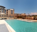 This contemporary apartment complex in Corinth, Texas, offers a blend of luxury and comfort. The exterior showcases a mix of brick and modern finishes, creating an appealing aesthetic. The centerpiece of the community is a resort-style pool area, complete with a pristine swimming pool featuring fountains and ample deck space. Surrounding the pool are numerous lounge chairs for sunbathing and relaxation.

The property boasts multiple outdoor living spaces, including a covered patio area with comfortable seating and dining options. These areas are perfect for socializing or enjoying the Texas weather. The complex features both open and covered balconies, providing residents with private outdoor spaces.

Interior common areas are designed with large windows, allowing natural light to flood in. The building's architecture includes interesting elements such as a cylindrical tower structure, adding visual interest to the facade. Well-maintained landscaping, including palm trees, enhances the overall ambiance of the property.

Inside, the apartments likely feature modern finishes and appliances, matching the upscale exterior. The complex appears to offer various amenities to cater to residents' needs, creating a comprehensive living experience in this Corinth, Texas location.