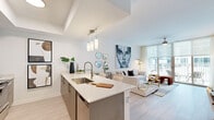 Located at 3750 S Dixie Hwy in Miami, FL, this well-appointed 1-bedroom, 2-bathroom residence offers a thoughtfully designed open-concept layout with modern finishes throughout. Light wood-tone flooring runs seamlessly across the living areas, complementing the bright, airy ambiance created by large floor-to-ceiling windows and roller shades that invite abundant natural light.

The kitchen is a functional centerpiece, featuring sleek gray cabinetry, a white quartz peninsula with bar seating, stainless steel appliances — including a French door refrigerator, range, and microwave — and a deep undermount sink with a designer faucet. Pendant lighting above the peninsula adds a refined touch. The kitchen flows directly into the open living area, where tray ceiling detailing adds architectural character.

The bedroom is generously proportioned, offering direct balcony access through sliding glass doors that frame outdoor views. A ceiling fan, soft natural light, and a well-sized closet round out the room's practical appeal.

Both bathrooms are clean and contemporary, with one featuring a glass-enclosed walk-in shower with full-height tile surround. Throughout the residence, the design palette of whites, warm neutrals, and brushed metals creates a cohesive, modern Miami aesthetic.