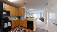 This single-floor residence offers a thoughtfully designed open-concept layout that seamlessly connects the kitchen, dining, and living areas. The kitchen is equipped with warm-toned wood cabinetry, a tile backsplash, black appliances including a refrigerator, range, microwave, and dishwasher, and a peninsula counter that serves as both a workspace and casual dining divider. Hardwood flooring anchors the kitchen and entry areas, while neutral carpet extends through the living and sleeping spaces.

The living room is bright and welcoming, featuring large multi-pane windows that frame views of the surrounding greenery and flood the room with natural light. Crown molding adds a refined architectural detail throughout. A dedicated dining area sits adjacent to the living room, creating a comfortable zone for everyday meals or entertaining.

The bedroom is a serene retreat highlighted by a soft accent wall, generous windows with outdoor views, plush carpeting, and access to a walk-in closet. The bathroom features large-format tile flooring, a white vanity with ample storage, a sizeable mirror, and a tub-shower combination. Overall, the space presents a clean, modern aesthetic with warm finishes and a cohesive, livable design.