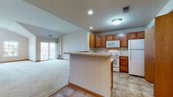 This single-floor residence at 12661 W Sycamore Dr in New Berlin, Wisconsin offers a well-organized layout with notable architectural details throughout. The living room serves as the centerpiece of the space, distinguished by soaring vaulted ceilings and an arched window that floods the area with natural light. A sliding glass door opens to a private balcony, extending the living space outdoors. Soft carpeting runs throughout the living and bedroom areas, contributing to a warm, comfortable atmosphere.

The kitchen is designed for functionality, featuring warm-toned wood cabinetry, white appliances including a range, built-in microwave, and refrigerator, along with a peninsula that provides additional prep space and a natural transition into the living area. Tile flooring throughout the kitchen adds durability and visual contrast.

The bedrooms are generously proportioned, each with plush carpeting, and select rooms include walk-in closets and windows with outdoor views. Two bathrooms serve the unit — one featuring a tub/shower combination with wood-toned vanity cabinetry, and the second offering a large mirror, single-sink vanity, and a separate shower, both finished with neutral tile flooring.