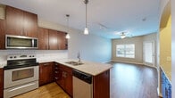 This single-story residence at 1501 NW 38th St in Kansas City, MO offers a well-designed open-concept layout that seamlessly connects the kitchen and living areas. The kitchen is a standout feature, equipped with rich dark-wood cabinetry, granite countertops, a white subway tile backsplash, and a full suite of stainless steel appliances including a refrigerator, range, microwave, and dishwasher. A peninsula with pendant lighting and a built-in sink adds both functionality and visual appeal, while hardwood-style flooring runs throughout the main living spaces.

The living area is bright and open, benefiting from natural light through large windows and a ceiling fan overhead. A private exterior door provides direct outdoor access. Arched architectural details add character to the hallways, which transition into carpeted bedroom spaces. The bedrooms are generously proportioned with vaulted ceilings, windows with natural light, and access to a walk-in closet. The bathroom features granite countertops with an undermount sink, dark wood vanity cabinetry, tile flooring, and a full tub-shower combination with tiled surround.