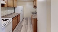 This single-floor residence offers a clean, functional layout designed for comfortable everyday living. The floor plan, as seen in the dollhouse view, reveals a thoughtfully organized arrangement of living, kitchen, bedroom, and bathroom spaces connected by an efficient corridor.

The living area features a combination of plush carpet and wood-look vinyl plank flooring, providing a warm transition between spaces. A ceiling vent ensures consistent climate control throughout the open area, which flows naturally toward the rest of the home.

The galley-style kitchen is equipped with warm-toned wooden cabinetry, granite-look countertops, a stainless steel sink, and a full-size refrigerator. A tile backsplash adds a subtle decorative touch, while the light vinyl plank flooring enhances the clean aesthetic of the space.

The bedrooms are carpeted and bathed in natural light from windows that offer views of surrounding greenery. One bedroom features a ceiling fan with a light fixture, while the other includes a flush-mount ceiling light — both providing practical comfort. Neutral wall tones throughout create a calm and versatile backdrop.

The bathroom includes a full-size soaking tub with an integrated shower, fitted with classic chrome fixtures and clean white surround panels. Overall, the space presents a tidy, move-in-ready environment with consistent finishes and a straightforward, livable design.