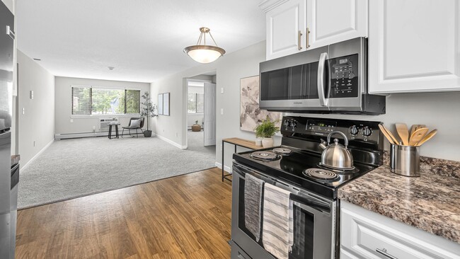 Experience dining joy in our contemporary kitchens, complete with modern, white cabinetry, stainless steel appliances and sleek wood-style flooring. - Country Manor