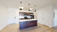 Located at 2386 W Spring Dr in Ozark, Missouri, this single-story home offers a thoughtfully designed open-concept layout filled with contemporary finishes throughout. Light wood-tone flooring runs continuously across the living spaces, creating a cohesive and airy feel.

The kitchen serves as a central hub of the home, anchored by a substantial island with a white countertop, double sink, built-in dishwasher, and seating overhang. Rich dark-stained cabinetry lines the walls, complemented by a white subway tile backsplash and a full suite of black appliances, including an electric range, over-the-range microwave, and stainless steel refrigerator. Three industrial-style pendant lights hang above the island, adding a modern touch.

The open living area flows directly from the kitchen and features recessed lighting, a ceiling fan, and a sliding glass door that brings in generous natural light and provides outdoor access. The bedrooms are bright and well-proportioned, each equipped with a ceiling fan and large windows that allow abundant sunlight. The bathrooms are clean and functional, featuring light-toned flooring, white surrounds, grab bars, and a combination of a walk-in shower in one bath and a shower-tub combo in another. The overall design reflects a clean, modern aesthetic suited for comfortable everyday living.